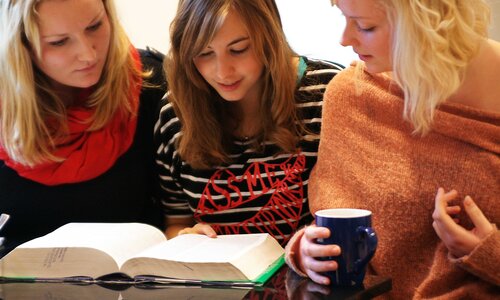 Drei Personen sitzen zusammen mit einem offenen Buch auf dem Tisch