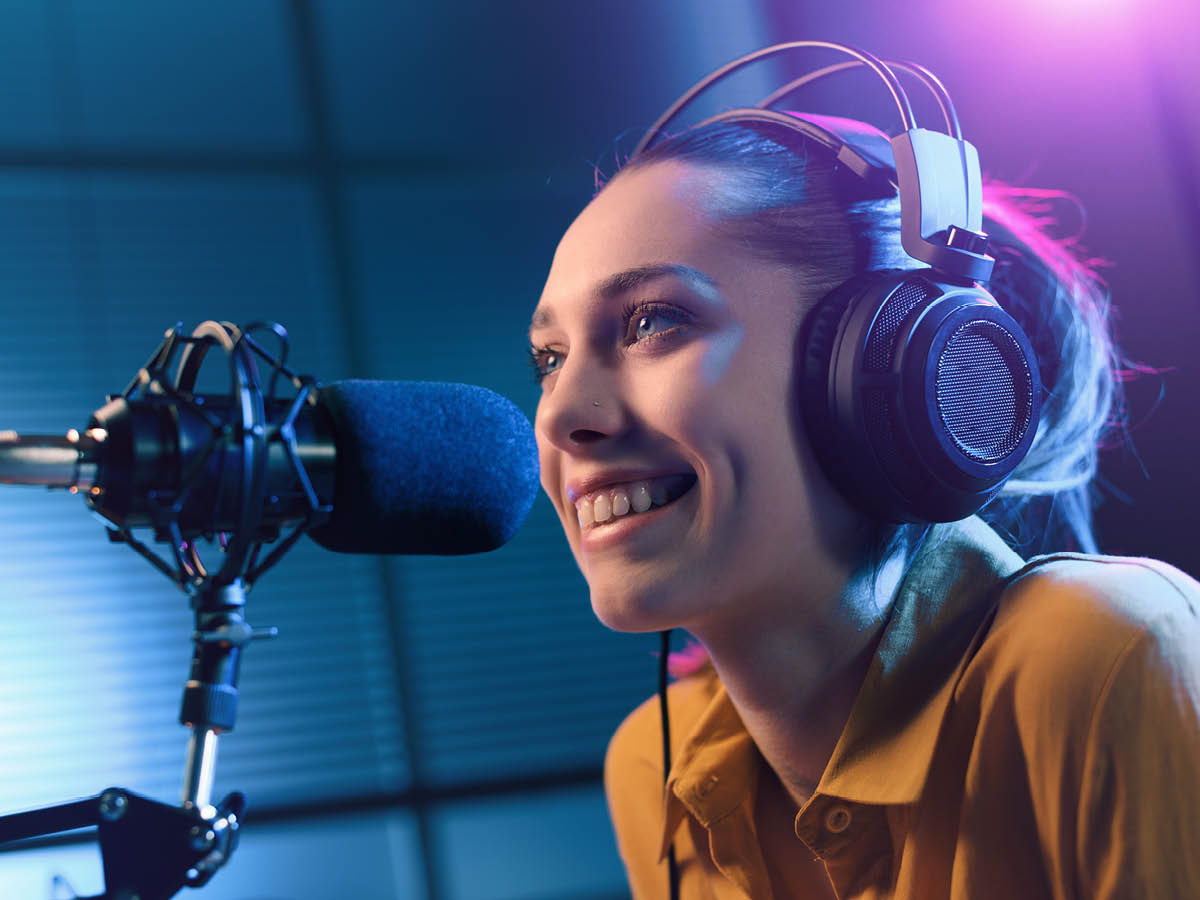 Eine Person trägt Kopfhörer und spricht in ein Mikrofon in einem Aufnahmestudio. 