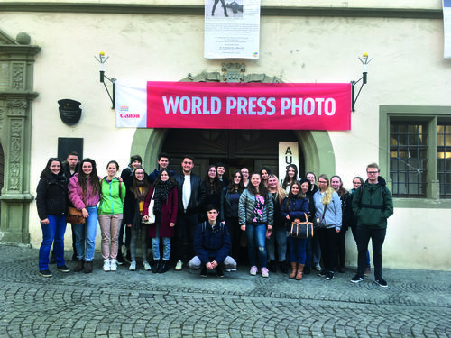 Gruppenbild unter Banner "WORLD PRESS PHOTO" Gruppe vor Gebäude mit rotem Banner WORLD PRESS PHOTO und der Aufschrift AULA über dem Eingang