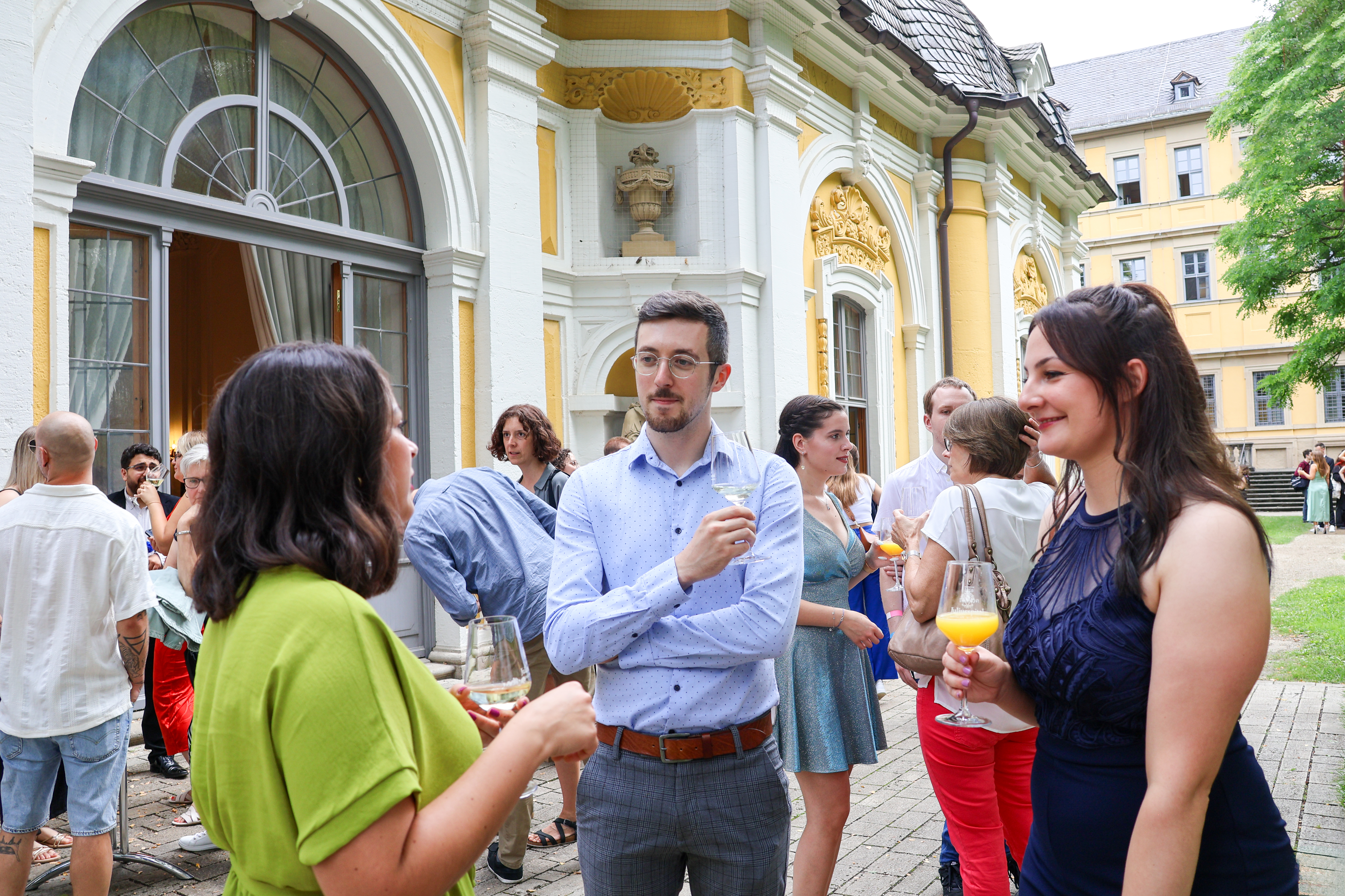 Feierlicher Sektempfang zur Zeugnisverleihung Menschen nach der Zeugnisübergabe bei einem geselligen Treffen vor einem historischen Gebäude mit Bögen und Verzierungen