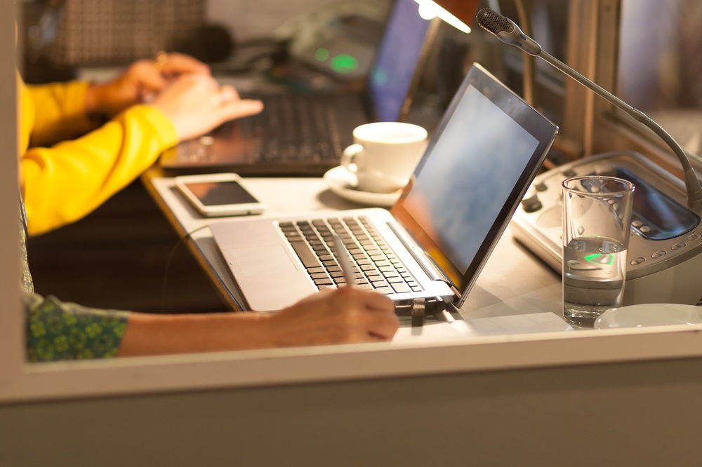 Zwei Personen arbeiten an Laptops an einem Schreibtisch mit Smartphone, Kaffee und Wasser