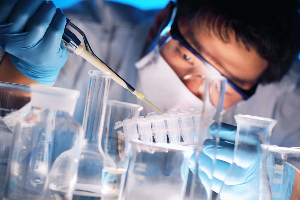 Wissenschaftler im Labor pipettiert Flüssigkeit in Reagenzgläser, umgeben von Laborgeräten