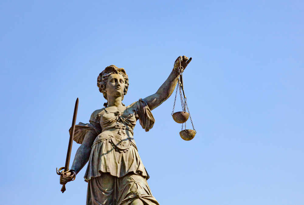 Statue der Justitia mit Schwert und Waage vor blauem Himmel